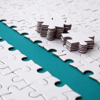 The blue path is laid on the platform of a white folded jigsaw puzzle. The missing elements of the puzzle are stacked nearby. Texture image with space for text photo
