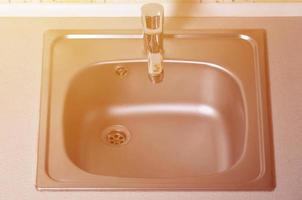 Empty clean silvery kitchen sink and water faucet close up photo