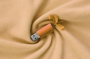Orange usb flash memory card with a bow lies on a blanket of soft and furry light orange fleece fabric with a lot of relief folds. Memory storage device in women's design photo