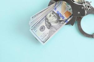 Silver police handcuffs and hundred dollar bills lies on light blue background photo