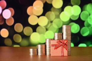 Small red gift box and golden coin stacks on the colored bokeh background photo