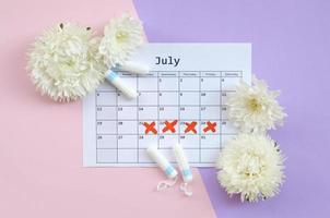 Menstrual tampons on menstruation period calendar with white flowers on lilac and pink background photo