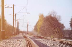 Autumn industrial landscape. Railway receding into the distance among green and yellow autumn trees photo