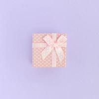 Small pink gift box with ribbon lies on a violet background. Minimalism flat lay top view photo