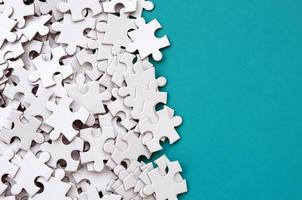 A pile of uncombed elements of a white jigsaw puzzle lies on the background of a blue surface. Texture photo with copy space for text