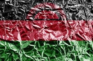 Malawi flag depicted in paint colors on shiny crumpled aluminium foil closeup. Textured banner on rough background photo