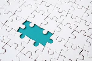 Close-up texture of a white jigsaw puzzle in assembled state with missing elements forming a blue pad for text. Copy space photo