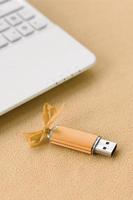 la tarjeta de memoria flash usb naranja con un lazo se encuentra sobre una manta de tela suave y peluda de color naranja claro al lado de una computadora portátil blanca. diseño clásico de regalo femenino para una tarjeta de memoria foto