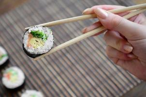una mano con palillos sostiene un rollo de sushi sobre un fondo de estera de paja de bambú. comida asiática tradicional
