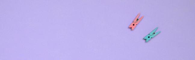 Two colored wooden pegs lie on texture background of fashion pastel violet color paper in minimal concept photo