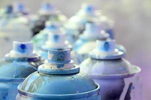 A lot of dirty and used aerosol cans of bright blue paint. Macro photograph with shallow depth of field. Selective focus on the spray nozzle photo