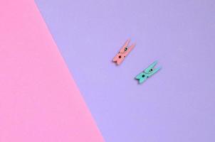 Two colored wooden pegs lie on texture background of fashion pastel violet and pink colors paper in minimal concept photo