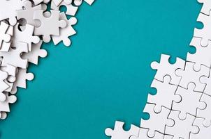 Fragment of a folded white jigsaw puzzle and a pile of uncombed puzzle elements against the background of a blue surface. Texture photo with space for text