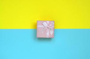 Small pink gift box lie on texture background of fashion pastel blue and yellow colors paper in minimal concept photo