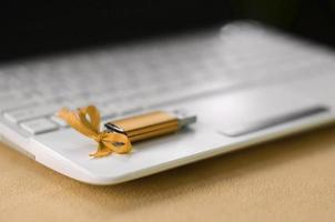 Orange usb flash memory card with a bow lies on a blanket of soft and furry light orange fleece fabric beside to a white laptop. Classic female gift design for a memory card photo