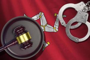 Isle of Man flag with judge mallet and handcuffs in dark room. Concept of criminal and punishment, background for judgement topics photo
