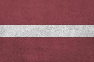 Latvia flag depicted in bright paint colors on old relief plastering wall. Textured banner on rough background photo