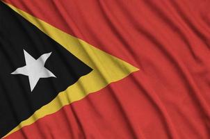Timor Leste flag  is depicted on a sports cloth fabric with many folds. Sport team banner photo