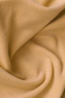 The blanket of furry orange fleece fabric. A background of light orange soft plush fleece material with a lot of relief folds photo
