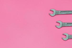 Three metallic spanners lie on texture background of fashion pastel pink color paper in minimal concept photo