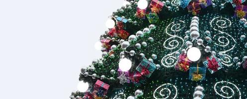 A fragment of a huge Christmas tree with many ornaments, gift boxes and luminous lamps. Photo of a decorated Christmas tree close-up with copy space