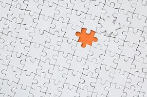 The texture of a white jigsaw puzzle in an assembled state with one missing element forming an orange space photo