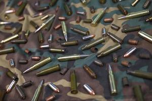 Many rifle bullets and cartridges on dark camouflage background photo