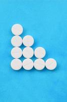 Several white tablets lie on a bright blue background in the form of a triangular arrow. Background image on medicine and pharmaceutical topics photo