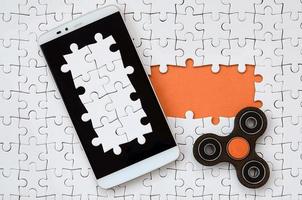 A modern big smartphone with a touch screen and a spinner lie on a white jigsaw puzzle in an assembled state with missing elements photo