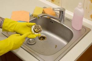 limpiador en guantes de goma muestra residuos en el protector de desagües de un fregadero de cocina foto