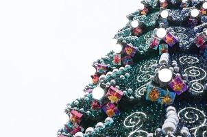 A fragment of a huge Christmas tree with many ornaments, gift boxes and luminous lamps. Photo of a decorated Christmas tree close-up with copy space