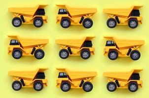 Many small yellow toy trucks on texture background of fashion pastel yellow color paper in minimal concept photo