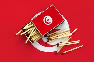 Tunisia flag  is shown on an open matchbox, from which several matches fall and lies on a large flag photo