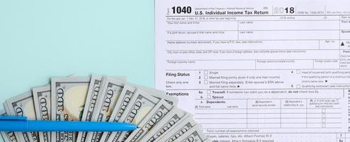 1040 tax form lies near hundred dollar bills and blue pen on a light blue background. US Individual income tax return photo