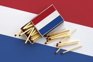 Netherlands flag  is shown on an open matchbox, from which several matches fall and lies on a large flag photo