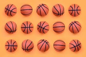 muchas pelotas naranjas pequeñas para el juego deportivo de baloncesto se encuentran en el fondo de textura del papel de color naranja pastel de moda en un concepto mínimo foto