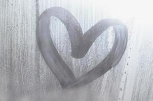 A heart-shaped drawing drawn by a finger on a misted glass in rainy weather photo