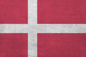 Denmark flag depicted in bright paint colors on old relief plastering wall. Textured banner on rough background photo