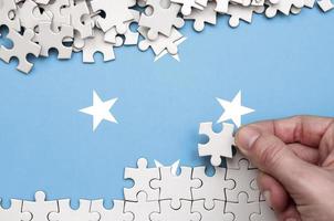 Micronesia flag  is depicted on a table on which the human hand folds a puzzle of white color photo