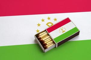 Tajikistan flag  is shown in an open matchbox, which is filled with matches and lies on a large flag photo