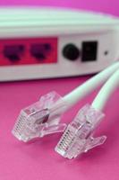 el enrutador de Internet y los enchufes del cable de Internet se encuentran sobre un fondo rosa brillante. elementos necesarios para internet foto