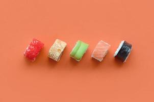 diferentes tipos de rollos de sushi asiáticos sobre fondo naranja. minimalismo vista superior plana con comida japonesa foto