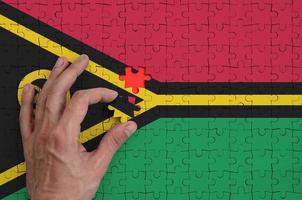 Vanuatu flag  is depicted on a puzzle, which the man's hand completes to fold photo