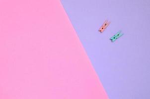 Two colored wooden pegs lie on texture background of fashion pastel violet and pink colors paper in minimal concept photo