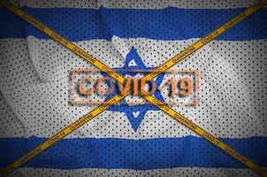 Israel flag and Covid-19 stamp with orange quarantine border tape cross. Coronavirus or 2019-nCov virus concept photo