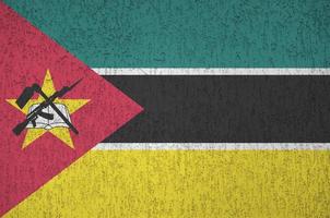 Mozambique flag depicted in bright paint colors on old relief plastering wall. Textured banner on rough background photo