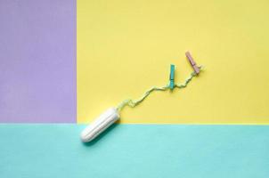 Tampon with two clothespins lie on texture background of fashion pastel violet, yellow and blue colors paper in minimal concept photo