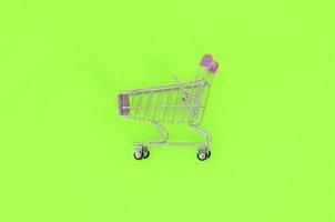 Shopping addiction, shopping lover or shopaholic concept. Small empty shopping cart lies on a pastel colored paper background. Flat lay minimal composition, top view photo