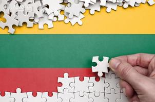 Lithuania flag  is depicted on a table on which the human hand folds a puzzle of white color photo