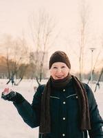 senior woman in hat and sporty jacket snowballing in snow winter park. Winter, age, sport, activity, season concept photo